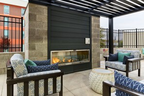 Un espace patio agrémenté d’une cheminée en verre, de mobilier d’extérieur et d’un mur en pierre.