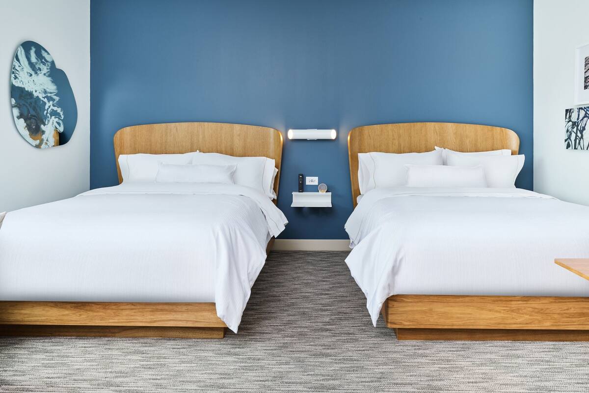 A hotel room with two beds, a nightstand, and a wall-mounted light fixture.