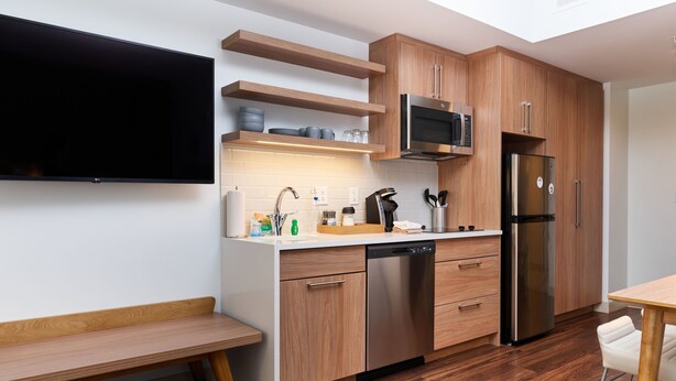 A modern kitchen with wooden cabinets, a stainless steel refrigerator, a microwave, and a dishwasher. - Element by Marriott Chattanooga East (Chattanooga)