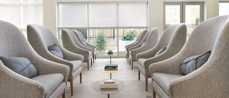 A seating area with six armchairs and a central coffee table, large windows, and a view of the outdoors.