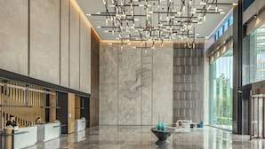Eine großzügige Lobby mit einer Rezeption, moderner Beleuchtung und einem großen Fenster mit Blick ins Freie.