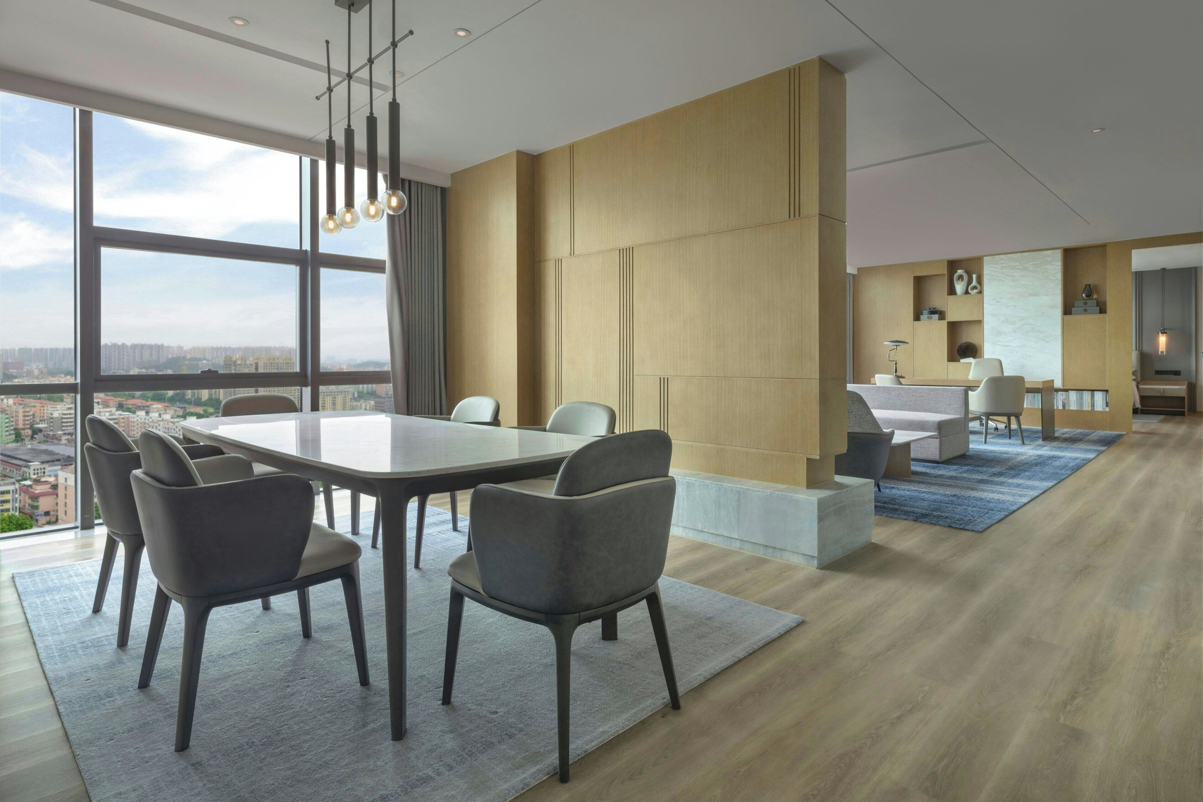 Une chambre d’hôtel moderne dotée d’une grande table à manger, de sièges confortables, d’un coin cuisine et offrant une vue sur le paysage urbain.