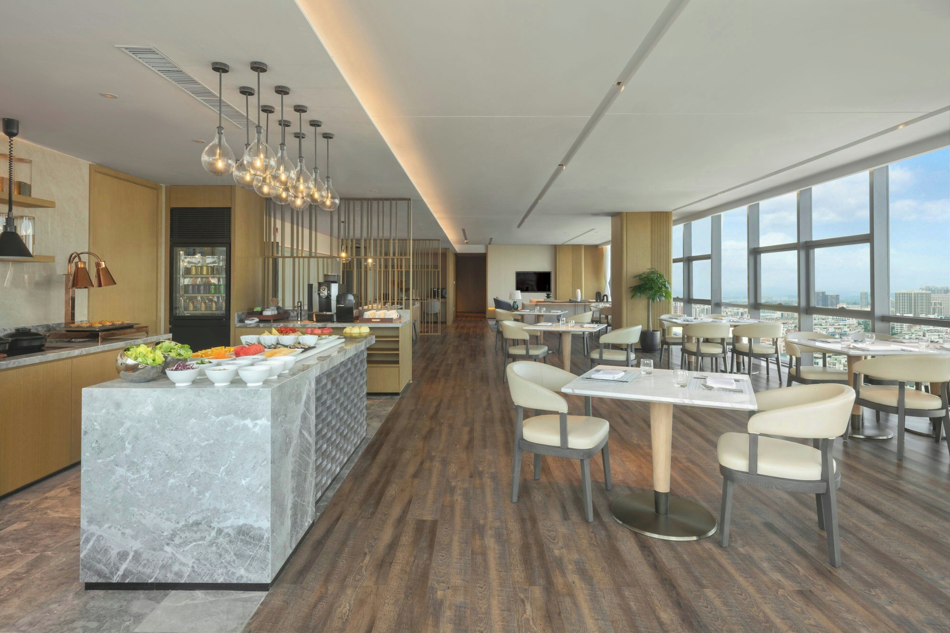 A modern hotel dining area with a marble bar, wooden flooring, and large windows offering city views.