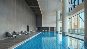 Ein moderner, überdachter Pool mit Fliesenboden, Liegestühlen und großen Fenstern mit Blick auf die Stadt.