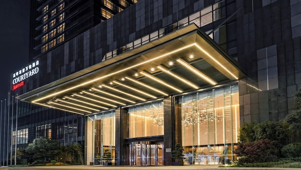 Ein moderner Hotelzugang mit Glasfassade, beleuchtetem Vordach und dem Courtyard Marriott Schild.