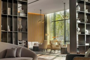 Una sala moderna con sofá, sillones, una estantería y un amplio ventanal.