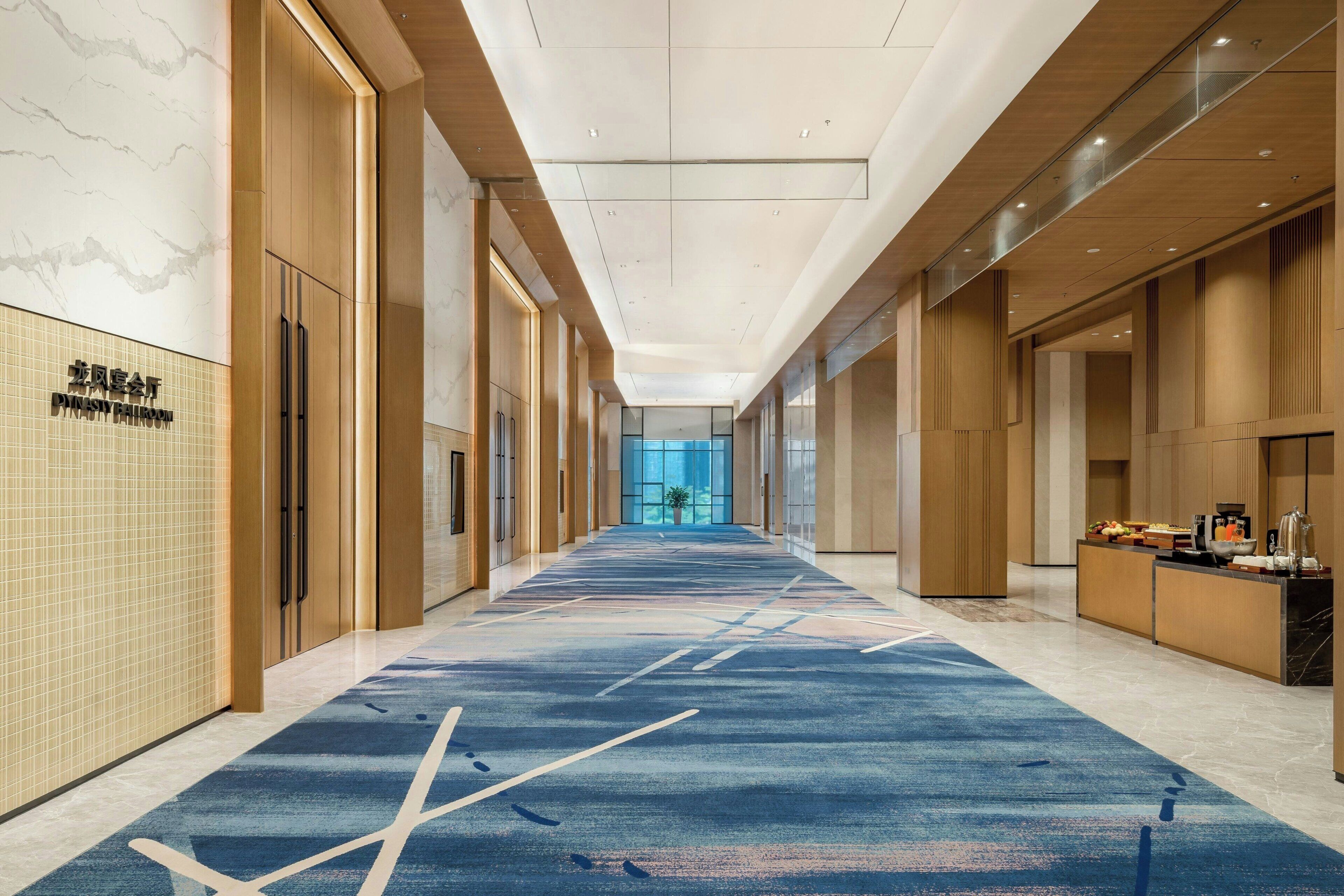 A hotel corridor with a blue carpet, wooden paneling, and a reception desk.