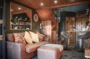 Un salon chaleureux avec un canapé en cuir, une table basse en bois et un coin repas agrémenté d’un tabouret de bar.