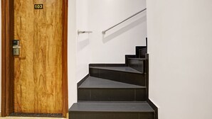 A wooden door with a number plate, a modern staircase with black steps, and a handrail. - Itsy Hotels Heraa International (Mumbai)