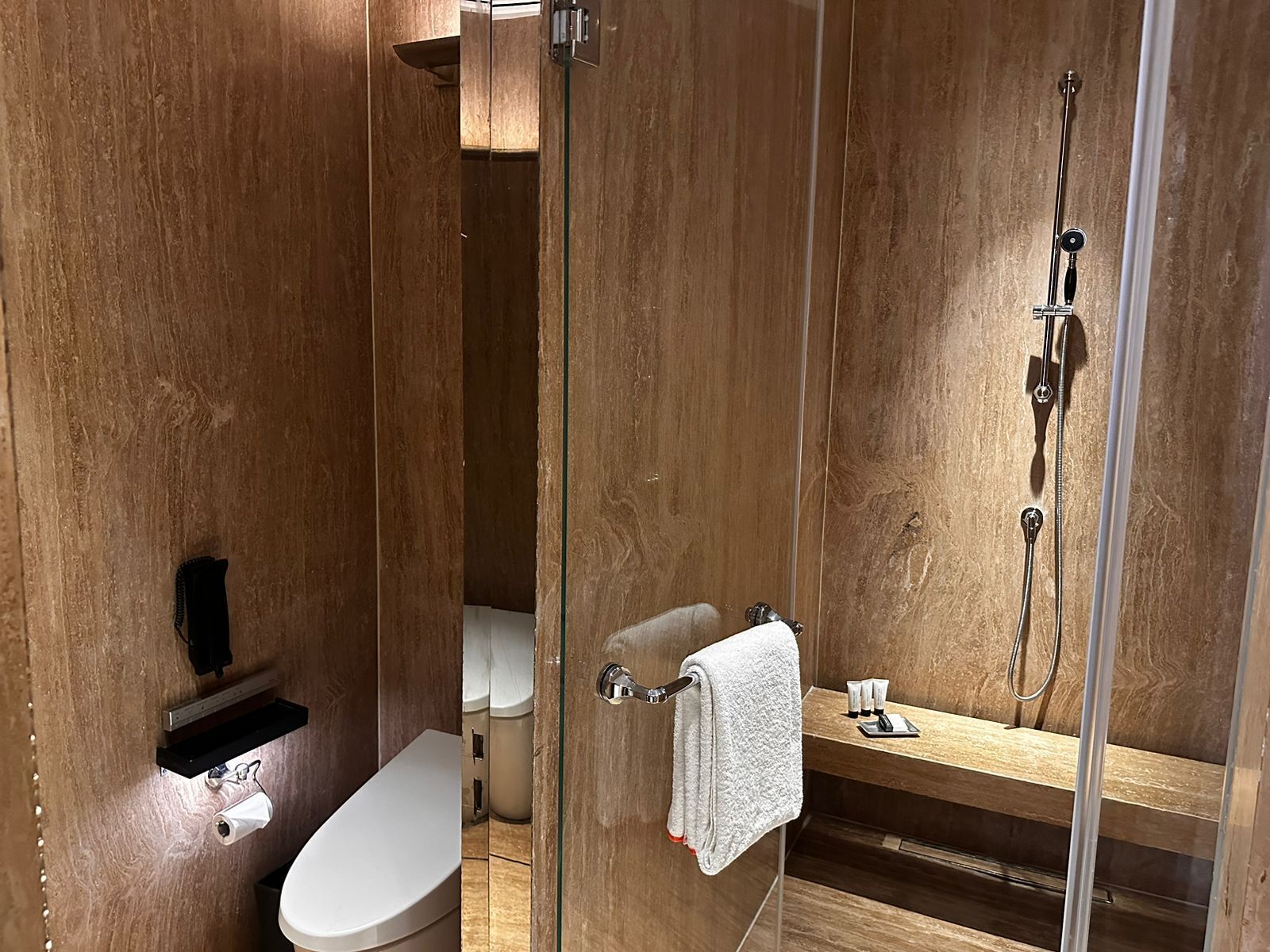 A modern bathroom with a glass shower enclosure, a toilet, and a vanity with toiletries.