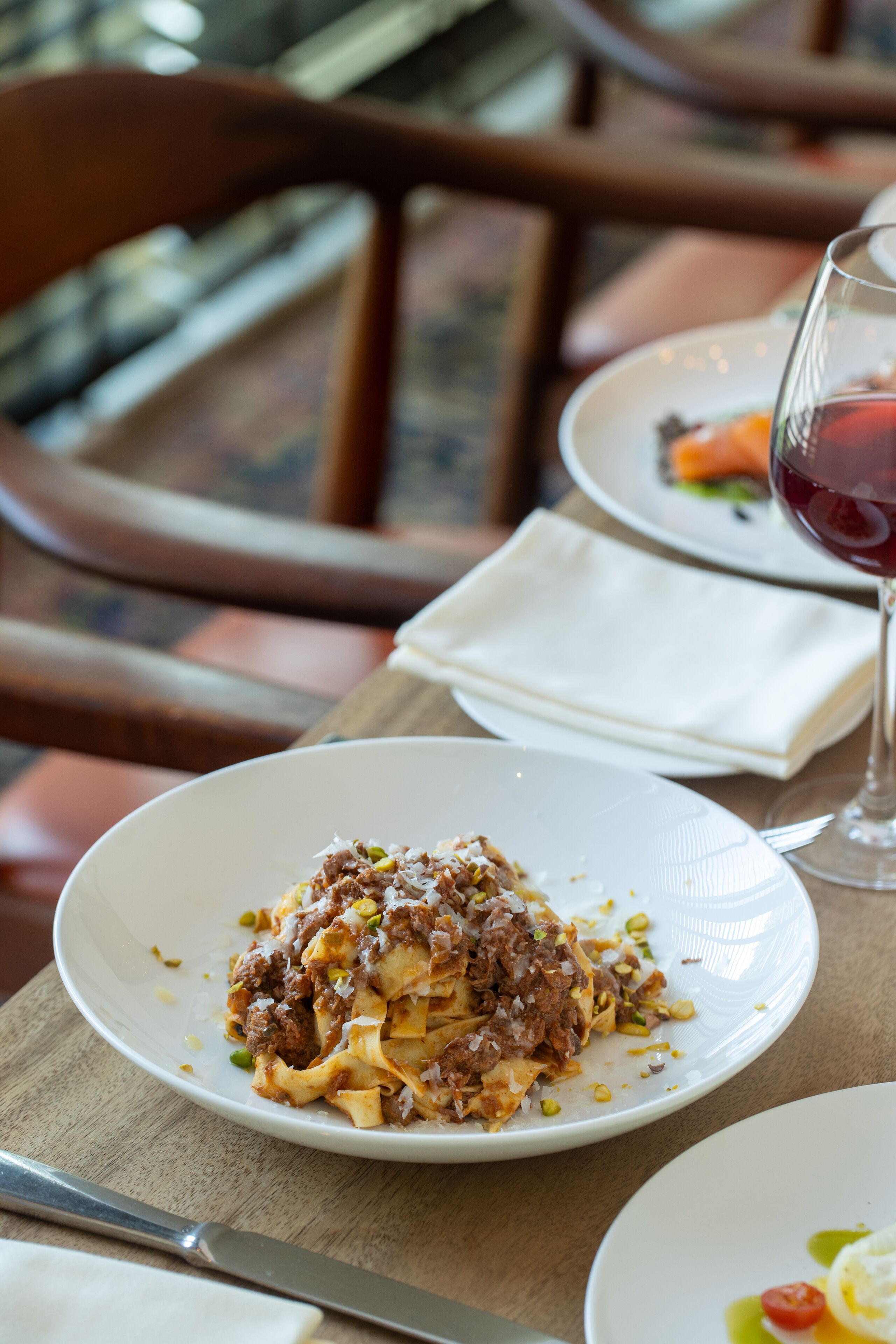 Une table à manger avec une assiette de pâtes, un verre de vin rouge et un couteau.