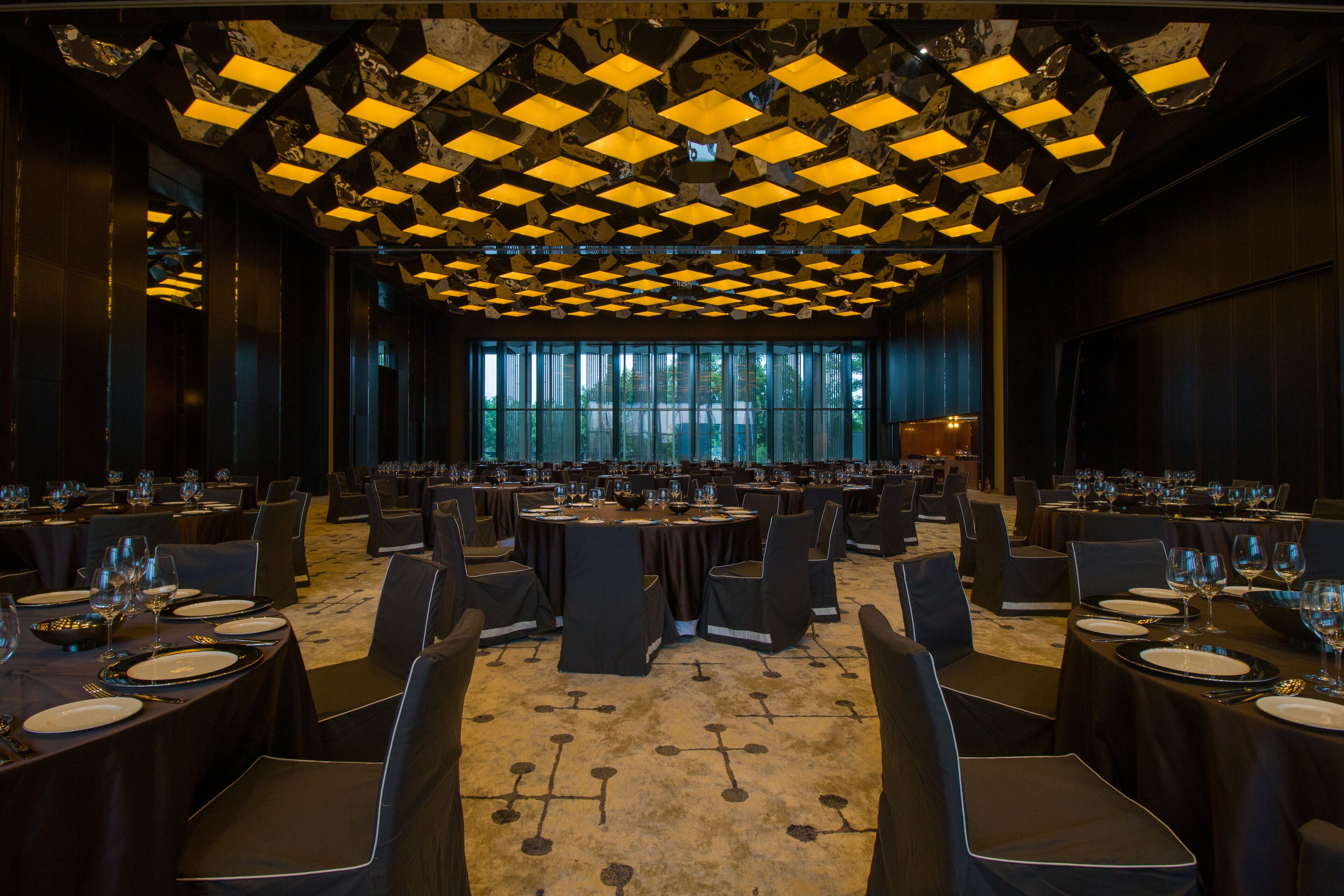 A conference room with multiple tables set for dining, large windows, and a patterned ceiling.