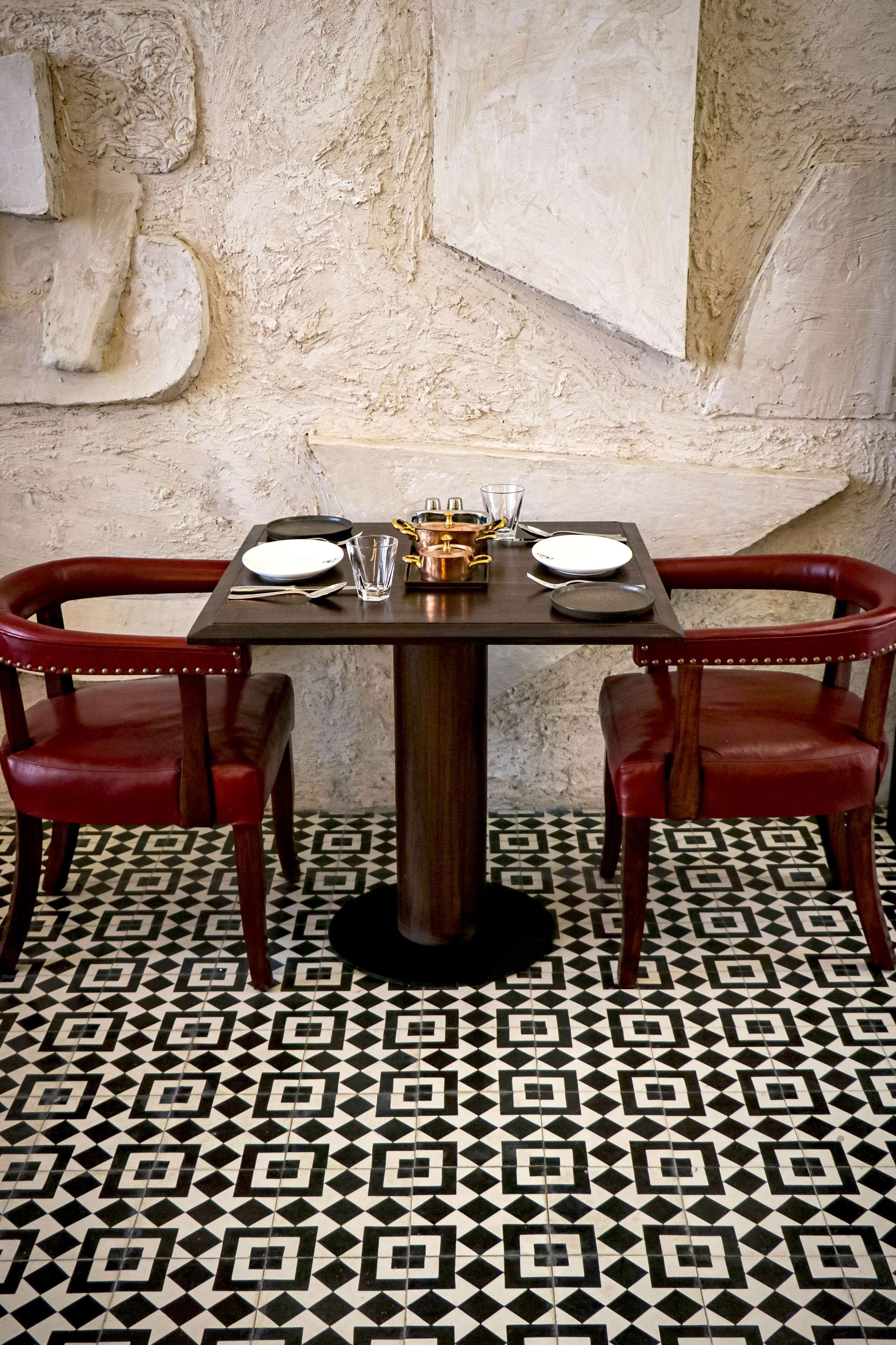 A dining area with a table set for two, two red upholstered chairs, and a patterned floor.