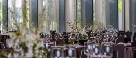 Une salle de banquet où les tables sont dressées pour un événement formel, avec des compositions florales et des verres à vin.