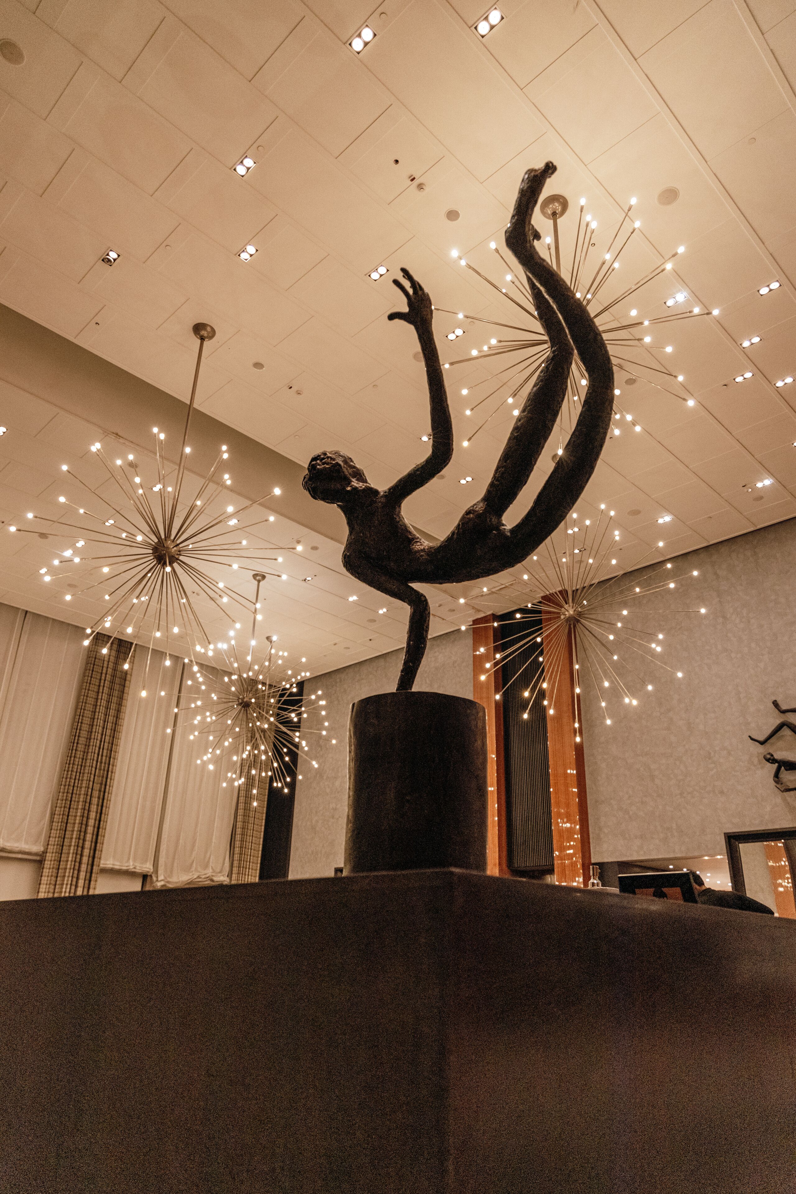 A sculpture of a person balancing on a pillar in a lobby with modern lighting fixtures and a high ceiling.