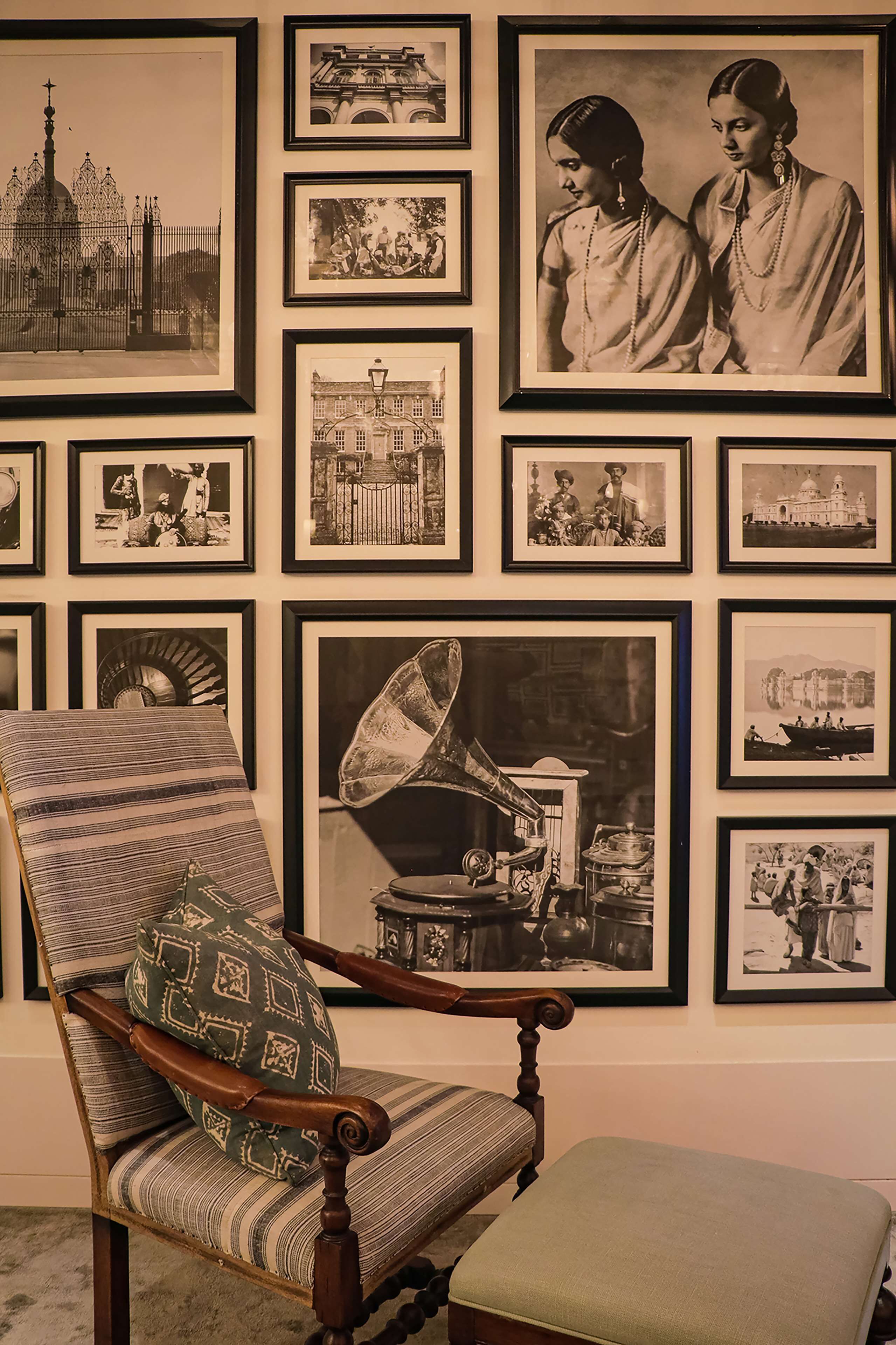 A room with a vintage chair, a framed photograph of a gramophone, and a wall adorned with various black and white photographs.