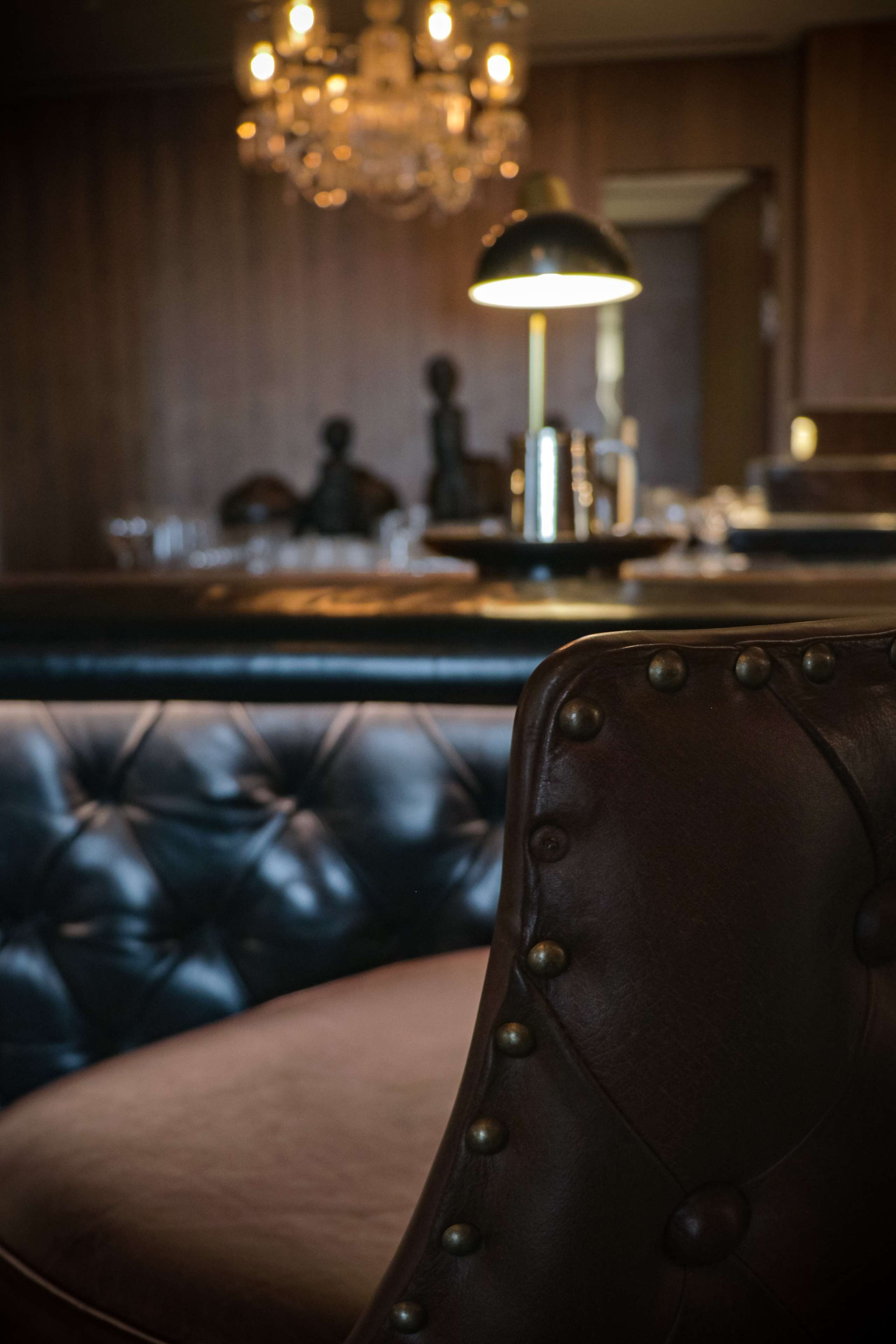 A leather armchair with rivets, a bar area with a lamp, and a chandelier in the background.
