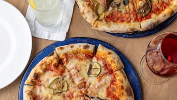 Dos pizzas sobre platos, un cuchillo, una servilleta y un vaso de agua en una mesa de madera.