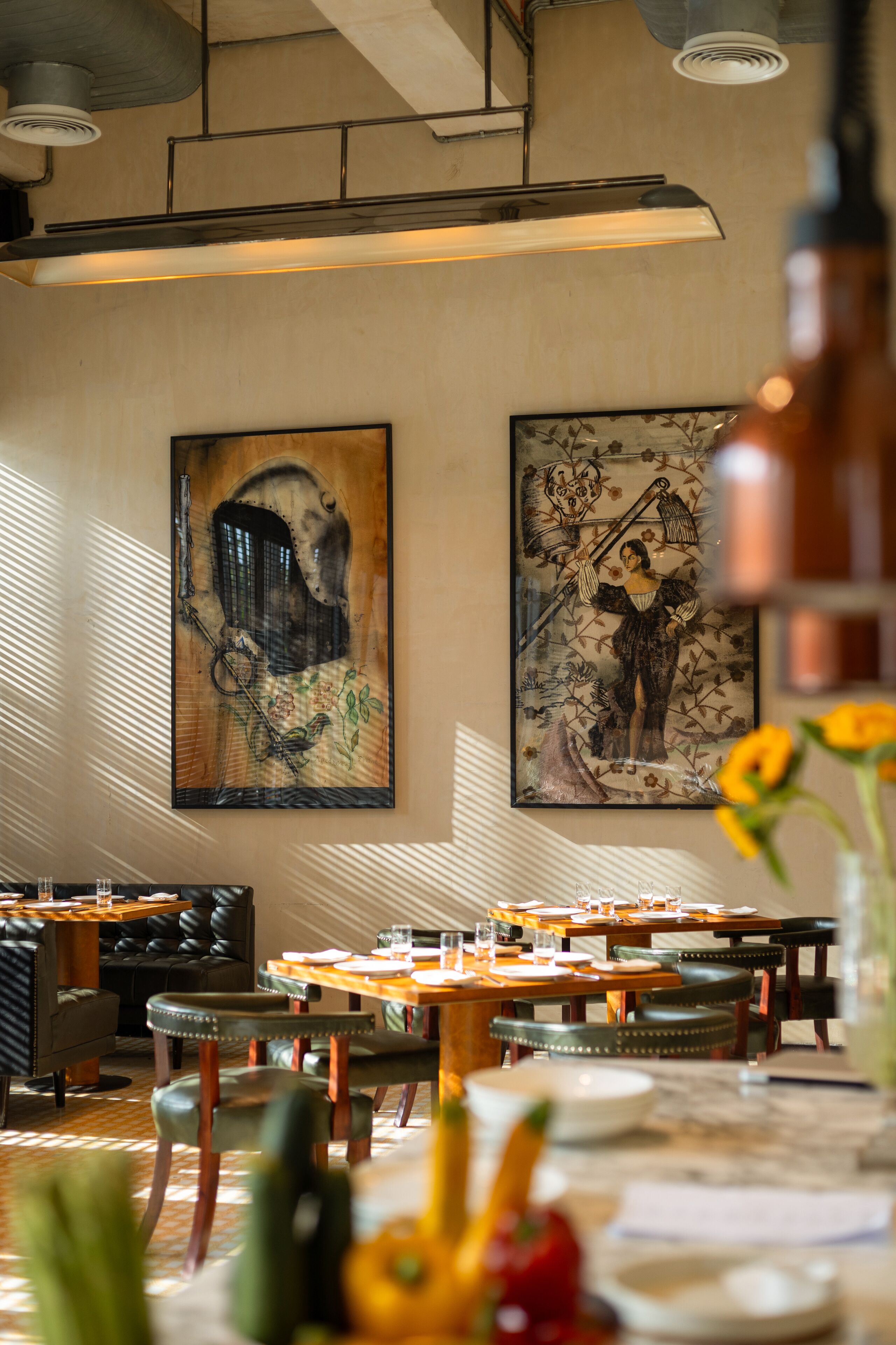 A dining area with tables and chairs, a large painting on the wall, and a ceiling light fixture.