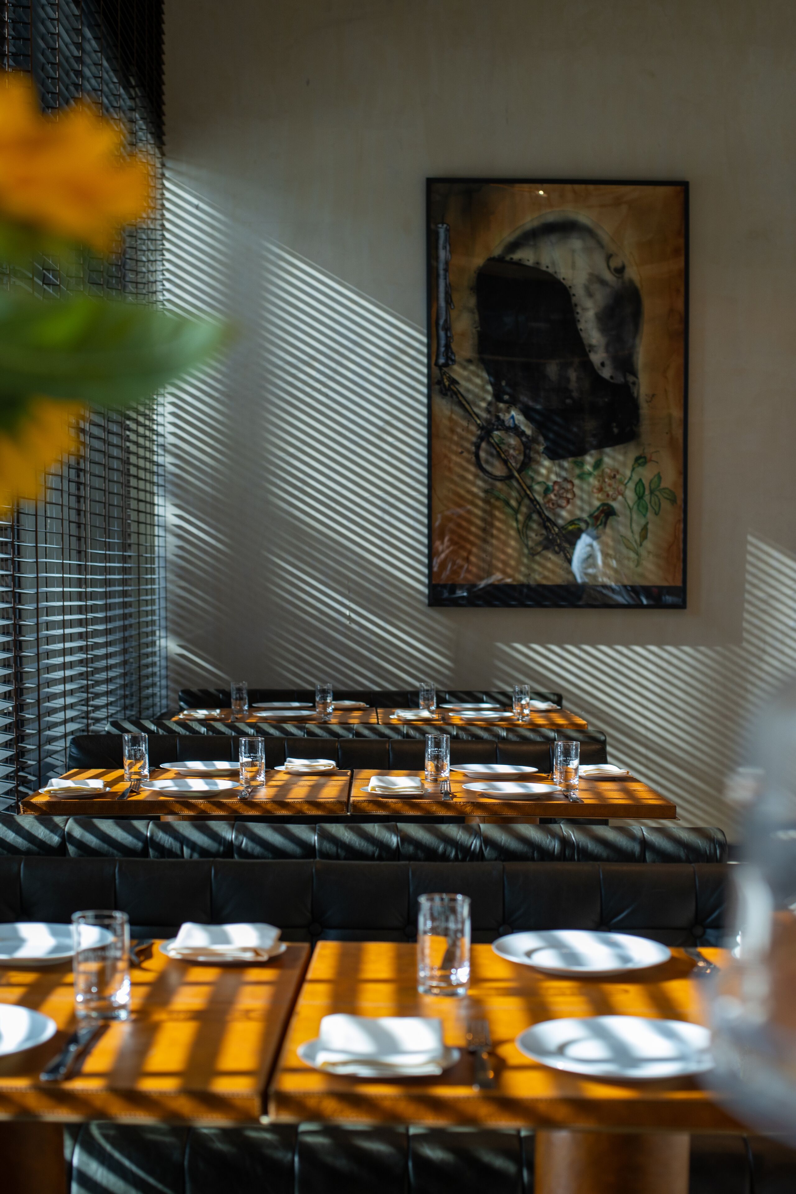 A restaurant with a modern interior, featuring leather seating and a large painting on the wall.