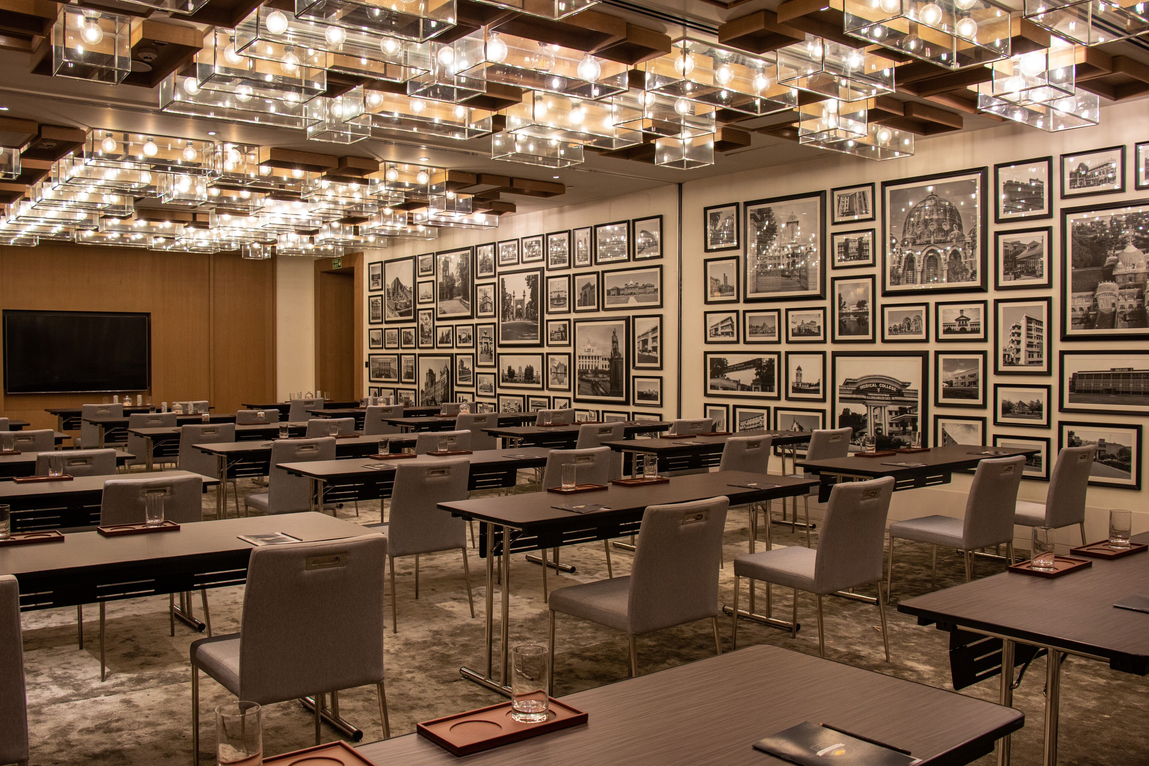 A conference room with multiple tables and chairs, a large screen, and a wall adorned with framed photographs.