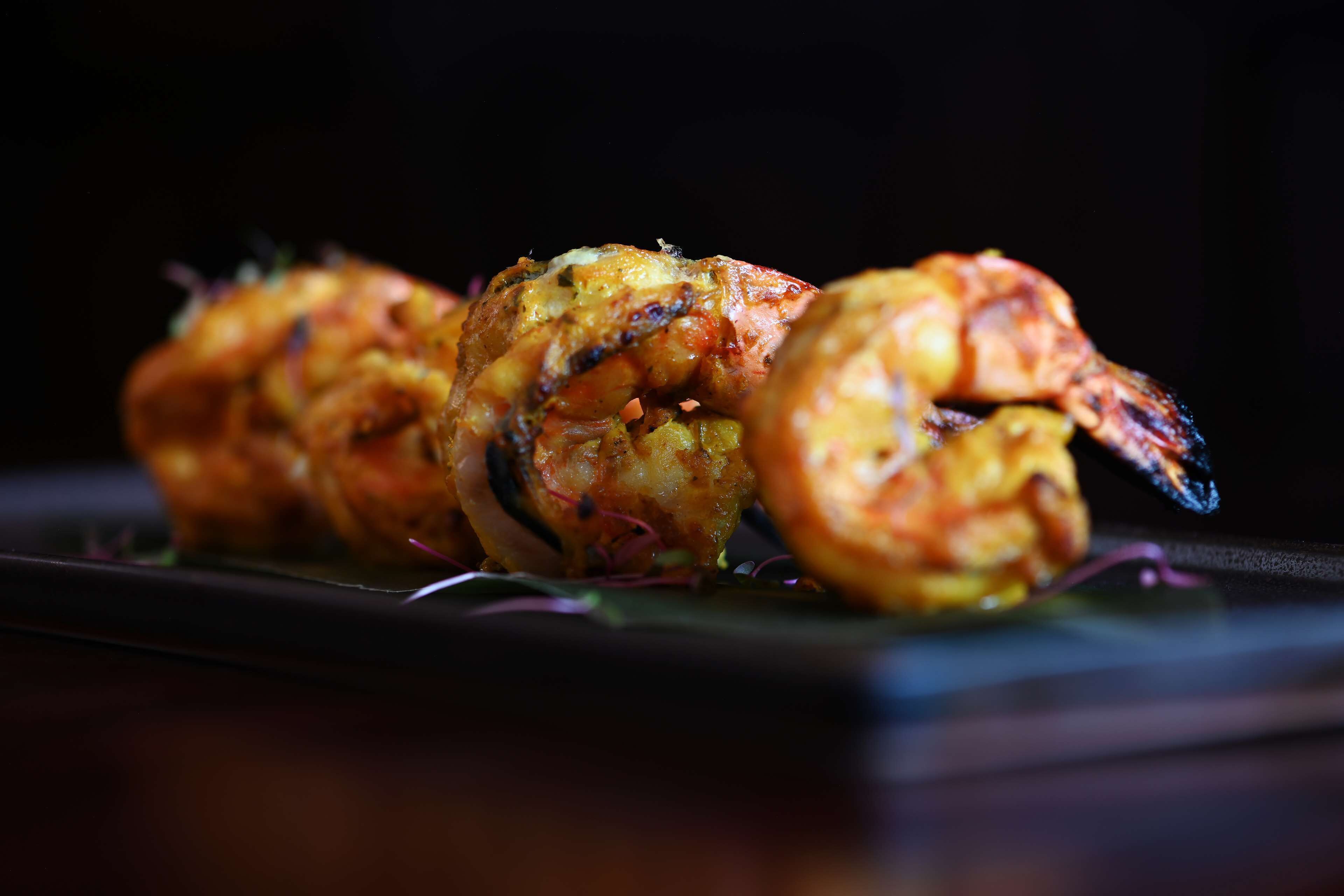 A close-up of a dish with skewered food items, possibly shrimp, on a dark plate.