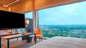 A hotel room with a large bed, a TV, a desk with a chair, and a view of a cityscape through large windows. - Grand Hyatt Gurgaon (Gurugram)