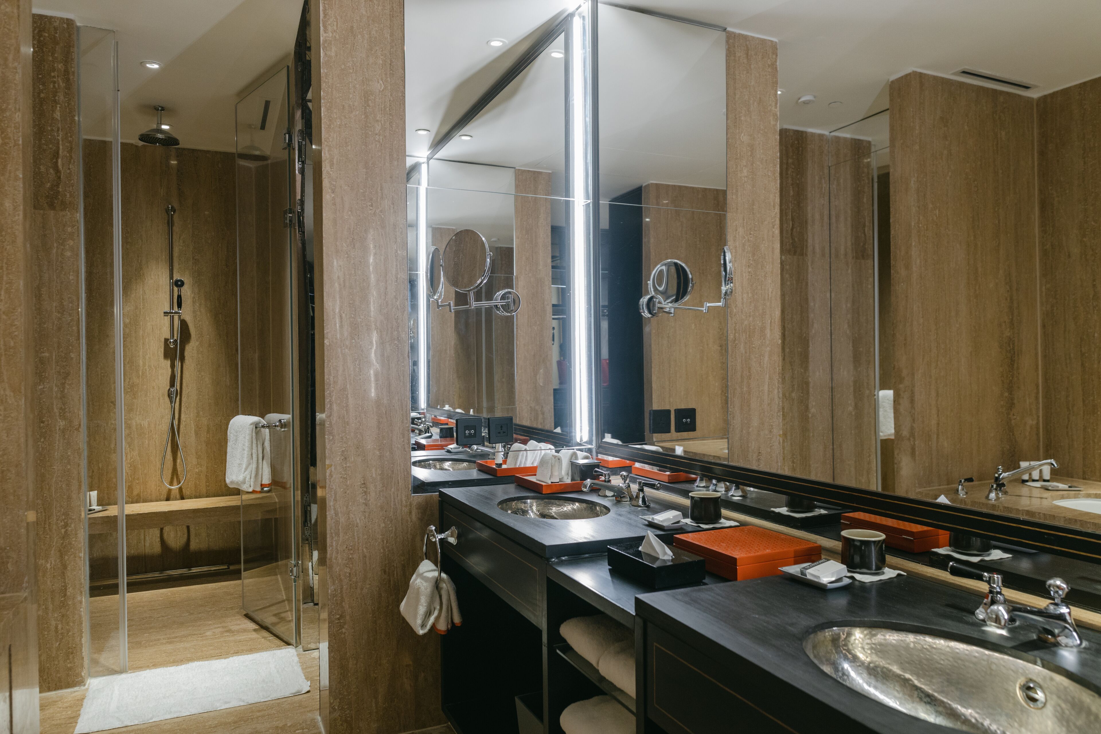 A modern bathroom with a glass-enclosed shower, a large mirror, and a vanity with two sinks and a countertop.