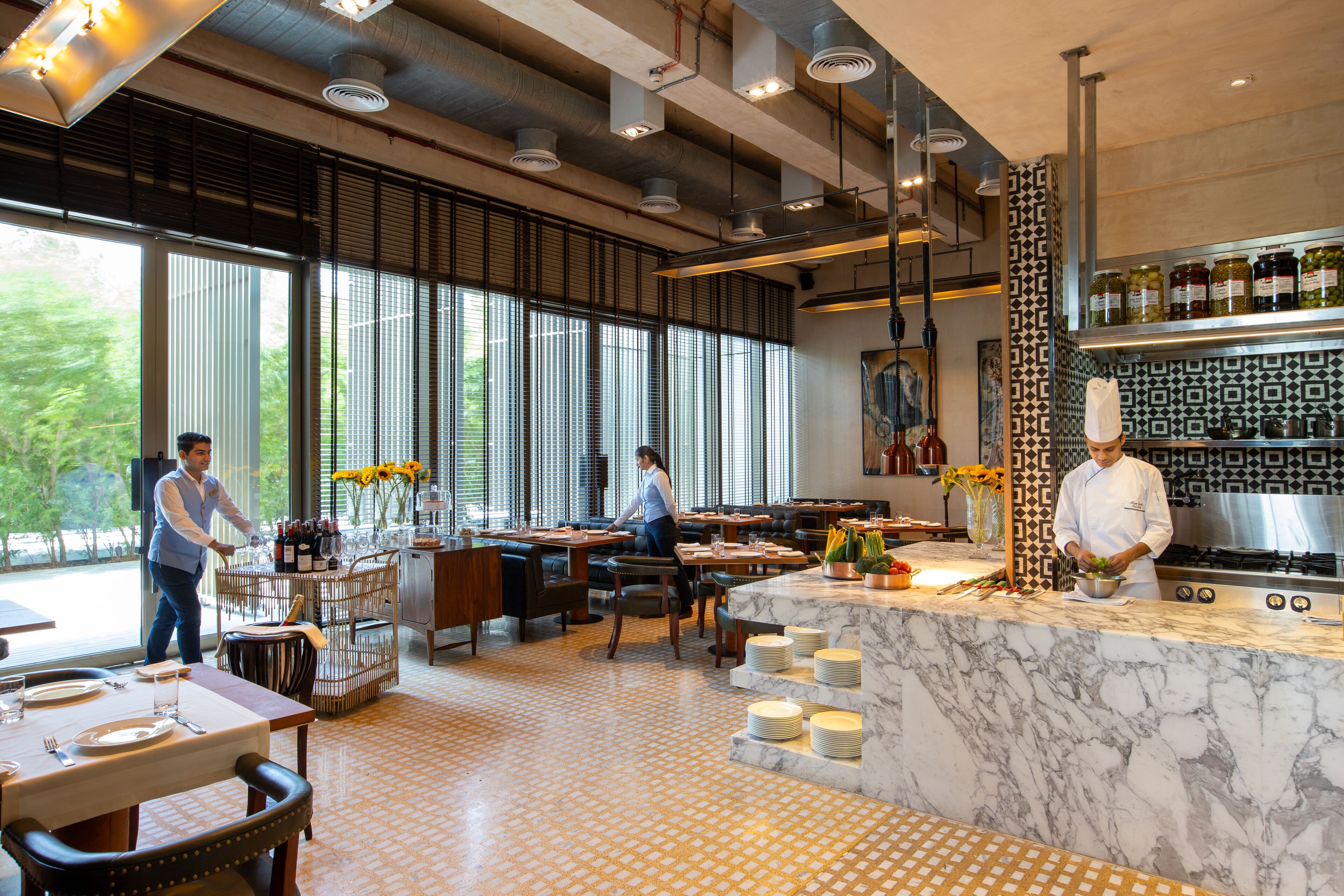 En modern restaurang med en bardisk i marmor, stora fönster och en kock som lagar mat.