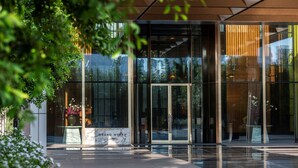 A modern hotel entrance with glass doors, a marble base, and greenery around. - Grand Hyatt Gurgaon (Gurugram)