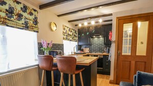 Una cuina moderna amb una illa central, dos tamborets de bar, una taula de dinar i un sofà.