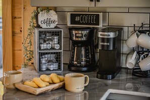 Una encimera de cocina con una cafetera, un cartel que dice “Pero primero, café” y una taza.
