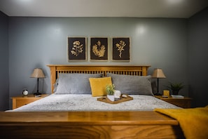 A neatly made bed with a wooden headboard, two bedside tables with lamps, and a tray with a plant and a cup.