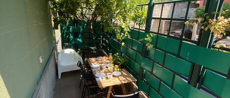 A covered outdoor dining area with a table set for two, surrounded by green fencing and potted plants.