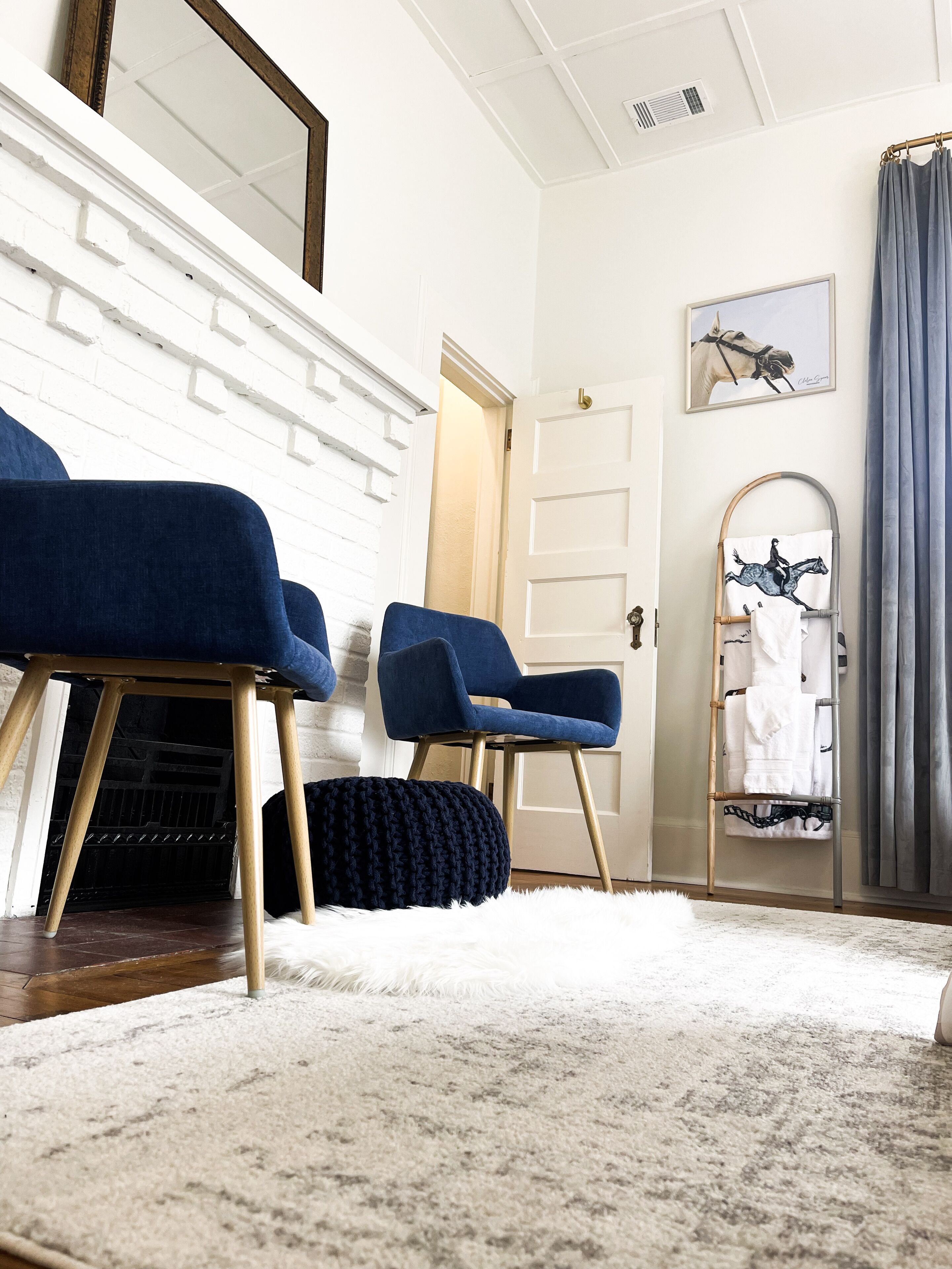 Een moderne woonkamer met een witte bakstenen muur, een houten trap en een grote spiegel. Er staan twee blauwe fauteuils en een zacht, wit vloerkleed.