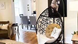 A living room with a hanging chair, a sofa, a dining area, and a wall-mounted picture. - Historic charm near downtown/Bruce's Field (Aiken)