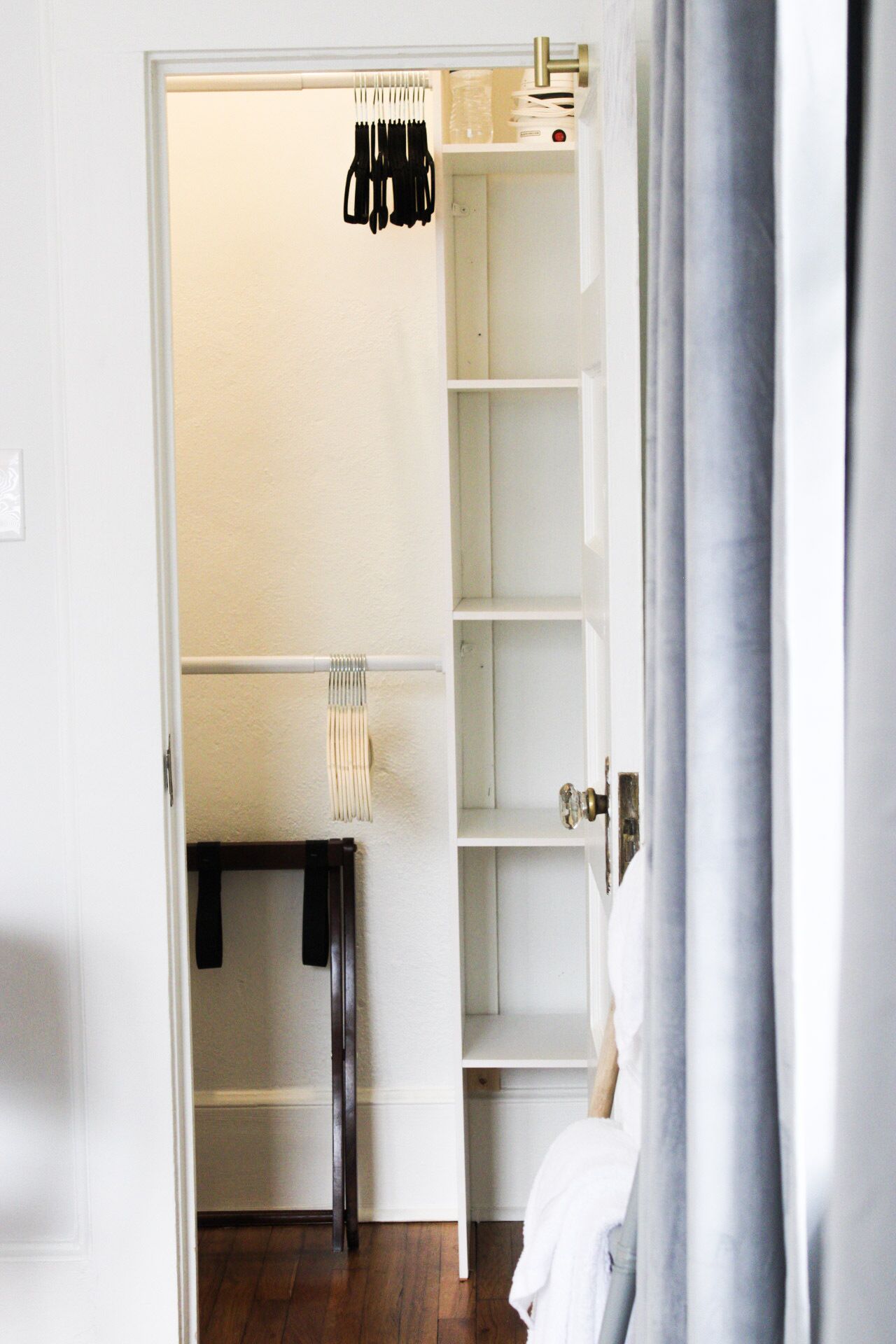 Ein begehbarer Kleiderschrank mit Kleiderstange, ein kleiner Tisch mit Lampe und ein Bett mit weißer Bettwäsche.