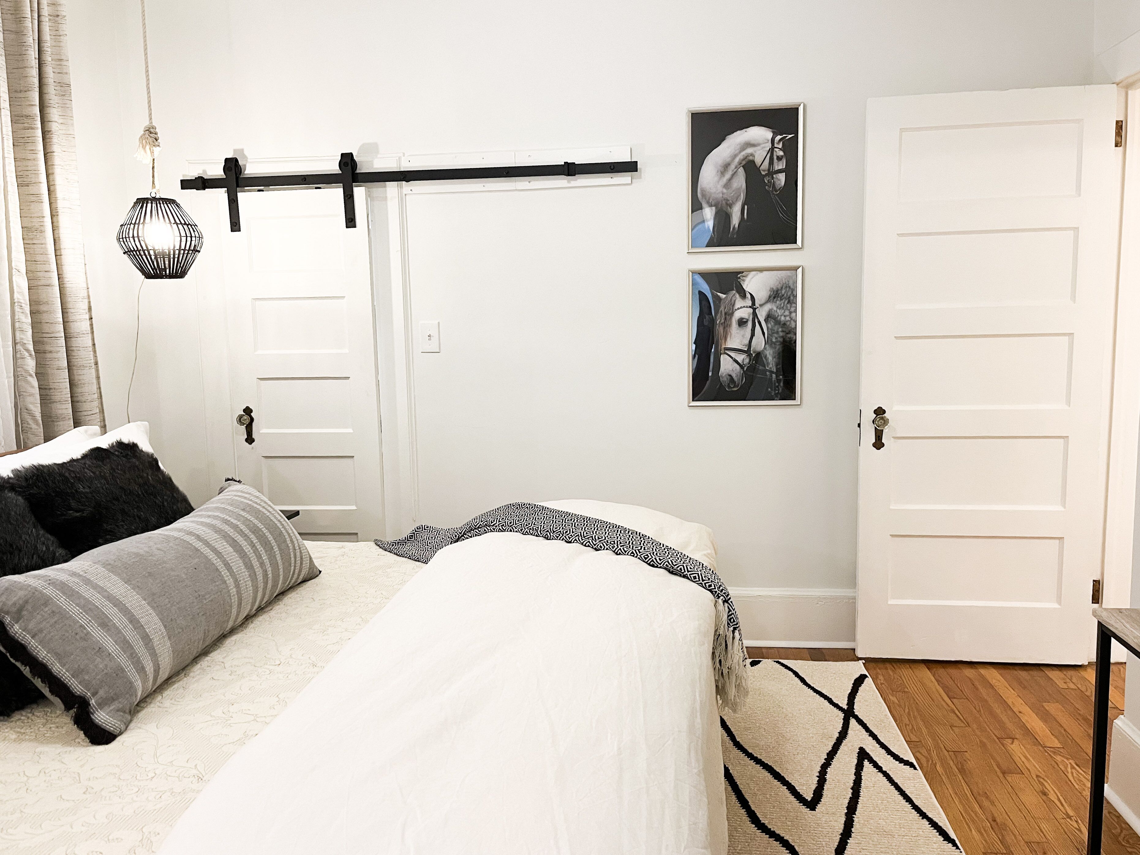 A bedroom with a bed, a hanging light fixture, and two framed pictures on the wall.