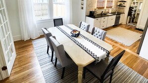 A dining area with a long table, chairs, a chandelier, and a kitchen in the background. - Historic charm near downtown/Bruce's Field (Aiken)
