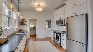 A modern kitchen with white cabinetry, a stainless steel refrigerator, a microwave, and pendant lights. - Historic charm near downtown/Bruce's Field (Aiken)