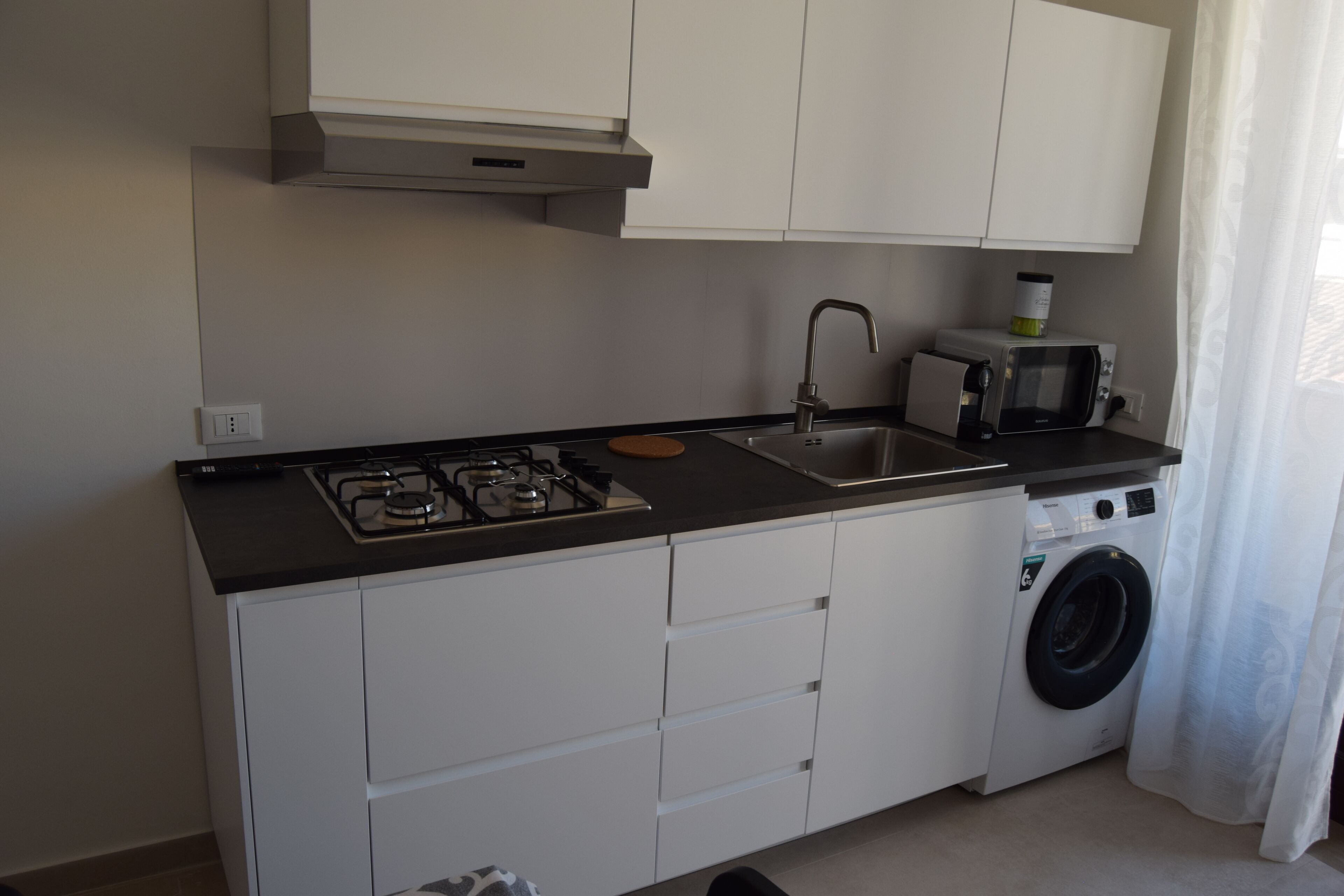 A compact kitchen with a gas stove, sink, microwave, and built-in washing machine.