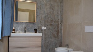 Un baño moderno con salpicadero de mármol, tocador de madera, lavabo blanco, un bidé y un inodoro.