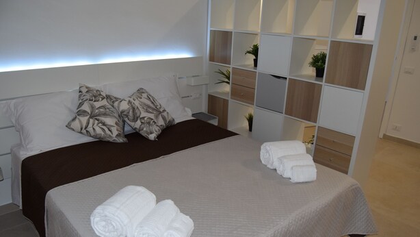 Una cama bien hecha con colcha blanca, dos almohadas y toallas enrolladas al lado.