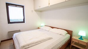 Un dormitorio con cama, mesitas de noche, una ventana y un armario en el techo.