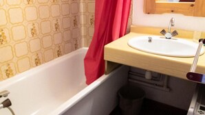 Un baño con una bañera blanca, un lavamanos con un espejo encima y un papel tapiz con diseño.