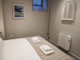 Un dormitorio con una cama, dos toallas, un radiador, una ventana y un cuadro en la pared.