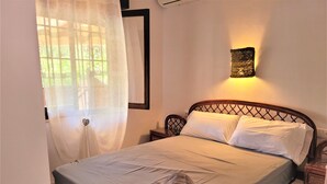 Un llit ben arrenjat amb una tovallola doblegada, una tauleta de nit amb una làmpada i una finestra amb cortines translúcides.