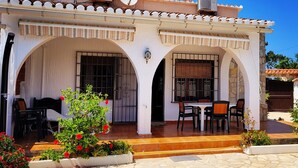 Edifici blanc amb teulada de rajola, dues arcades, un pati amb taula i cadires, i plantes en testos.