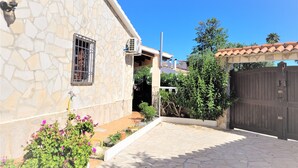 Una casa de pedra amb teulada de rajola, entrada tancada per una reixa i un jardí petit amb plantes florents.