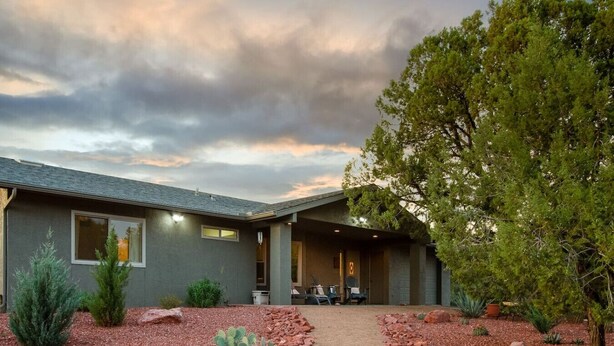 Una casa moderna con un patio cubierto, camino de grava y diversas plantas de desierto.